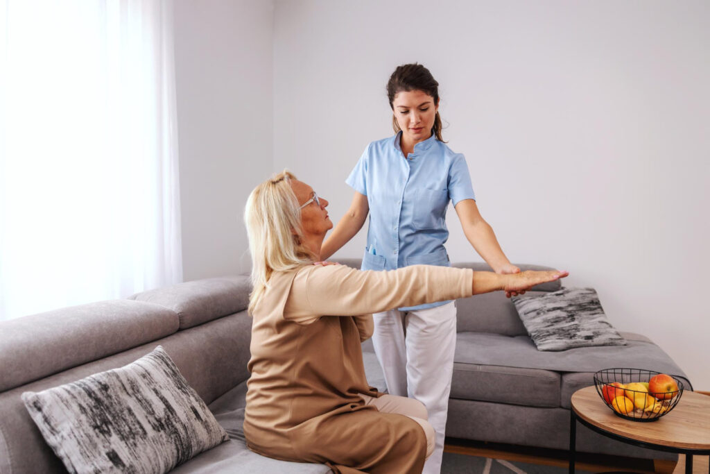 Senior woman sitting on couch with stretched arm while nurse checking on her arm